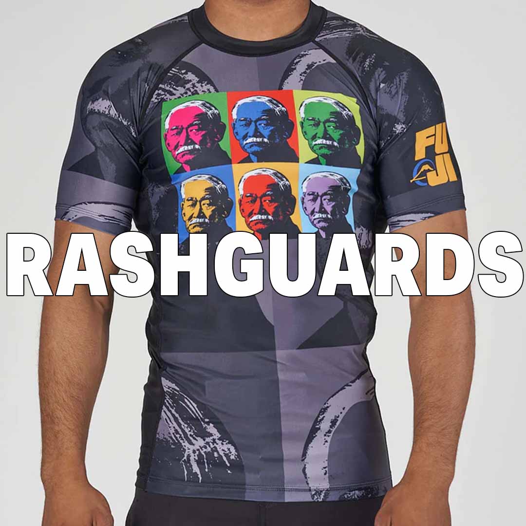 A person wearing a colorful rashguard with a pop art design featuring six portraits on the chest. Large white text across the image reads RASHGUARDS. The right sleeve has yellow text and a small logo.