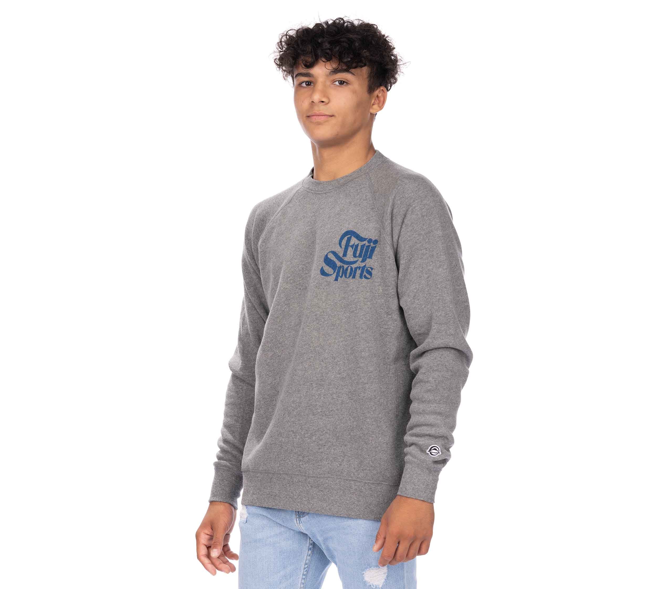 A young person with curly dark hair wears a gray Wave Crewneck Men's Sweatshirt and light blue ripped jeans, standing against a white background and looking slightly to the side.