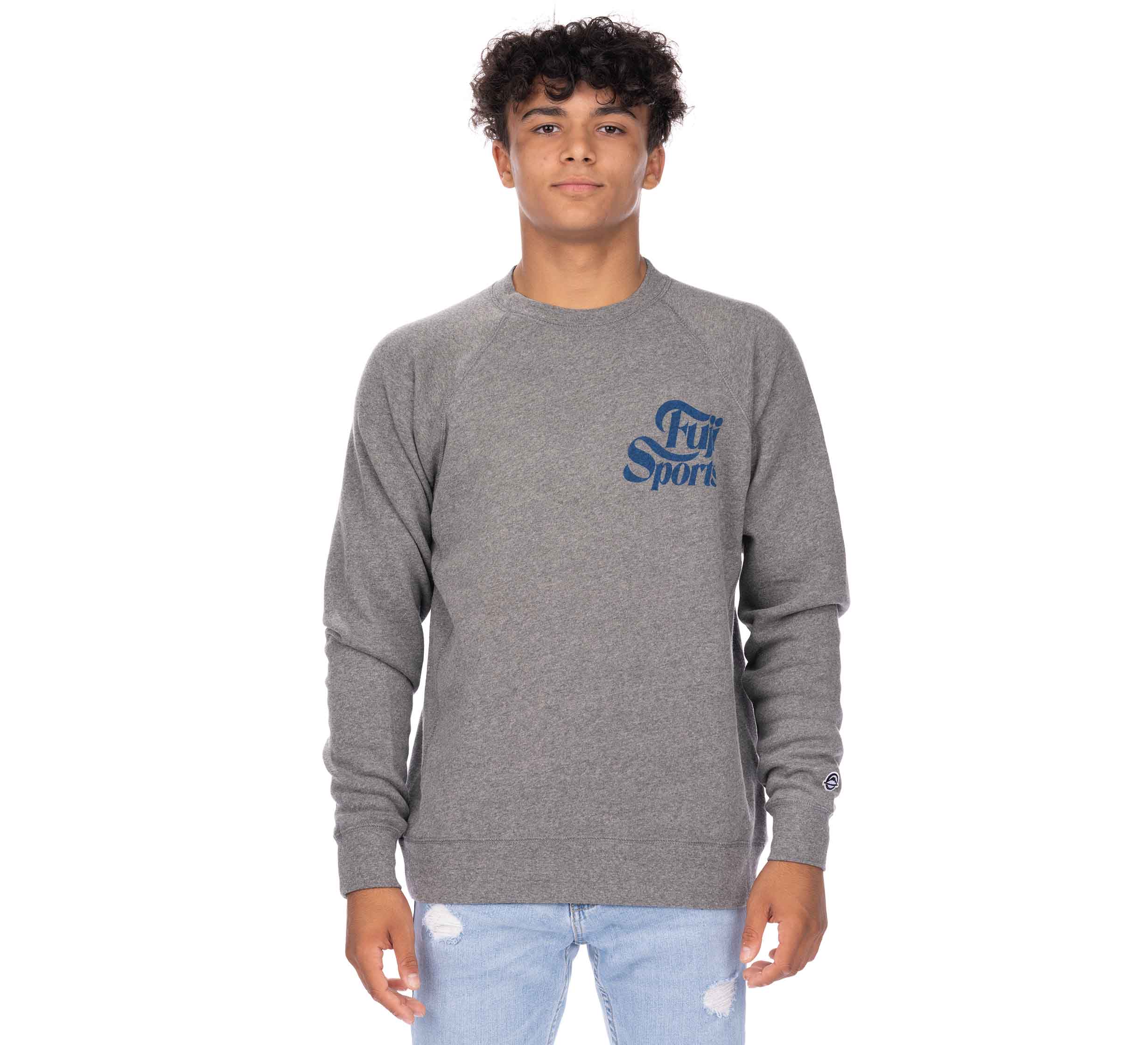 A young man with curly hair wears a Wave Crewneck Men's Sweatshirt in gray with "Fly Sports" printed in blue on the chest and light blue ripped jeans, standing against a plain white background.