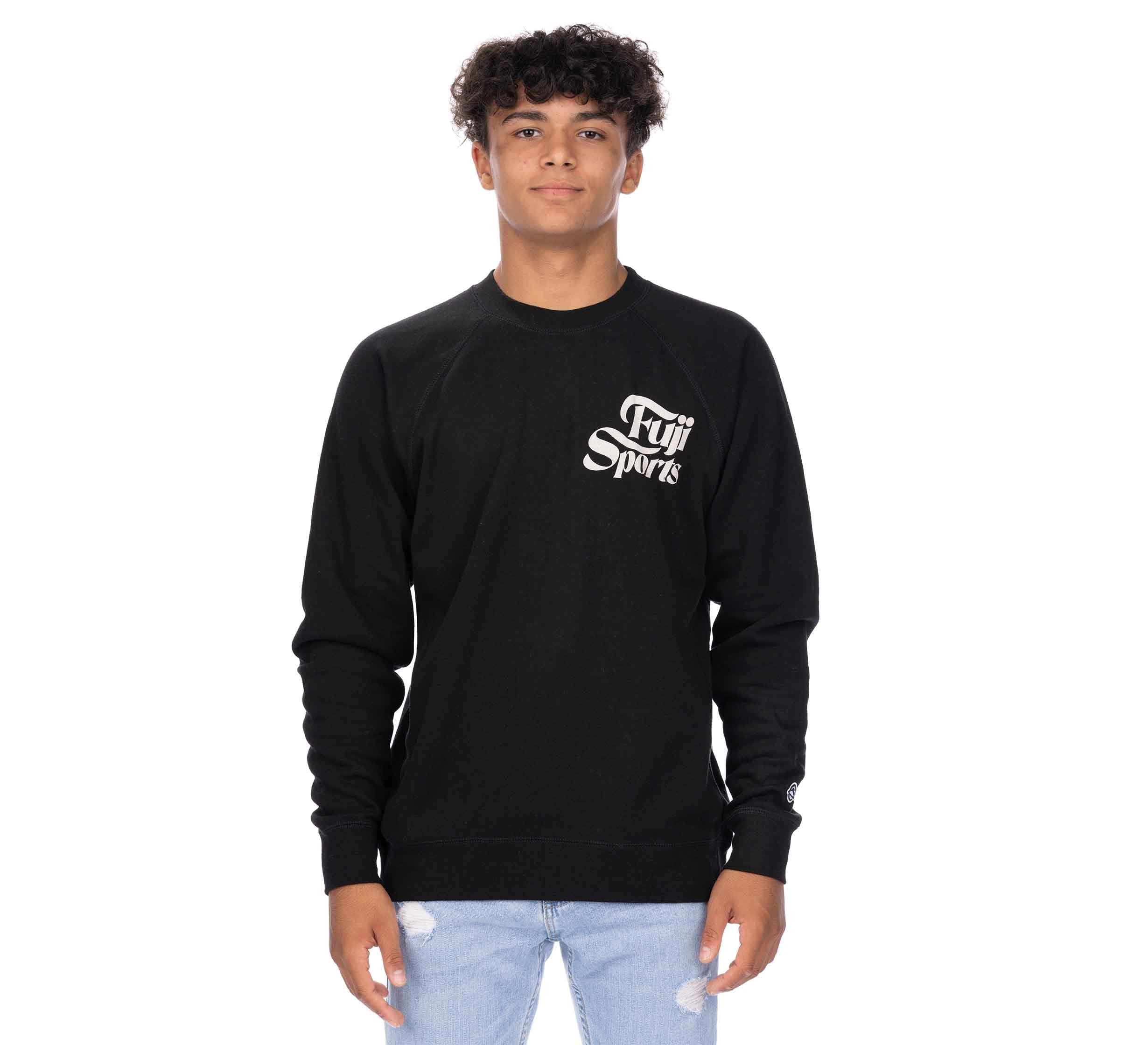 A young person with curly hair wears a black Wave Crewneck Men's Sweatshirt and light blue ripped jeans, standing against a plain white background.