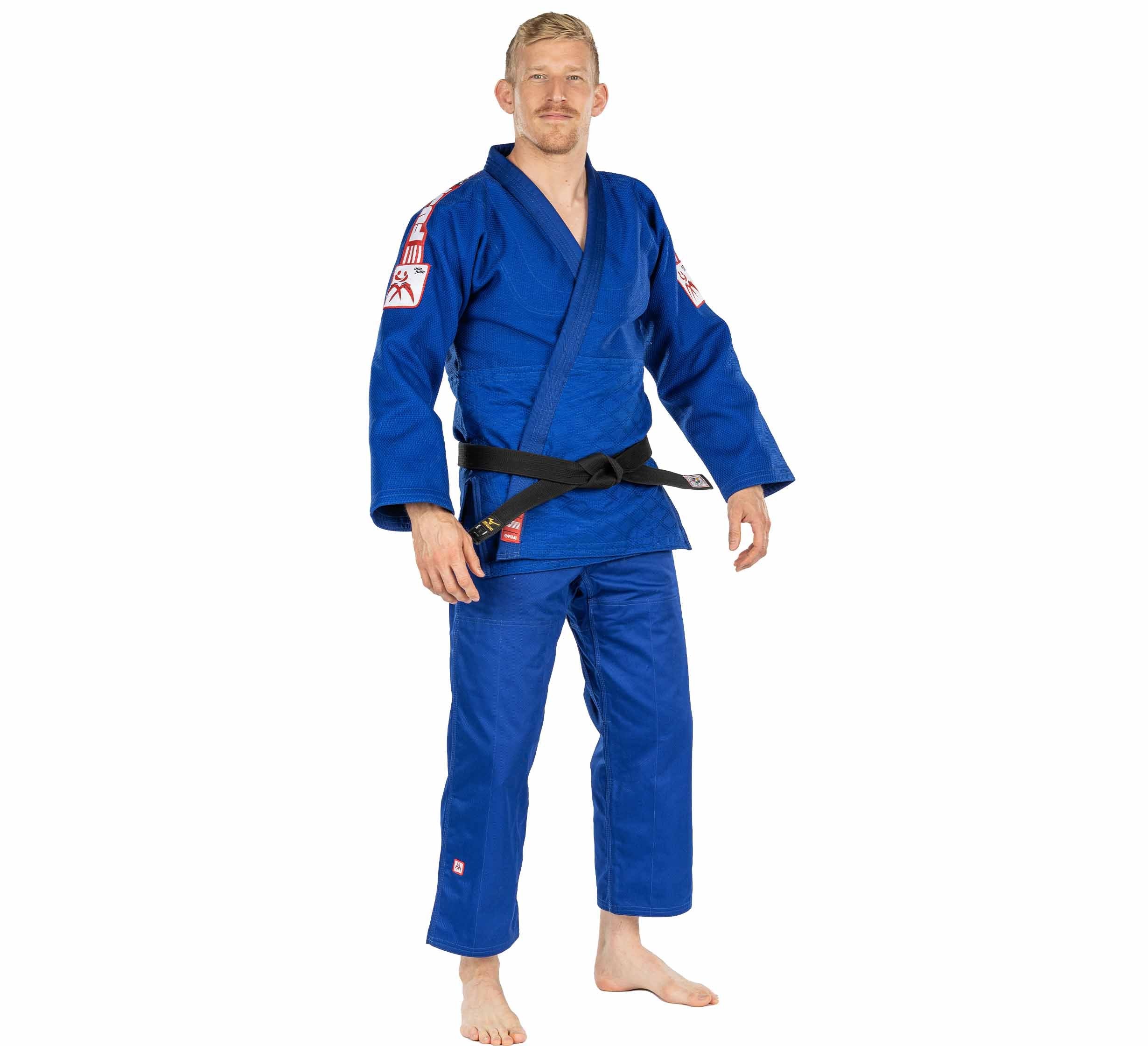A man stands barefoot against a white background, facing forward with a slight smile, wearing the USA Judo Double Weave Gi 2.0 Blue and a black belt.