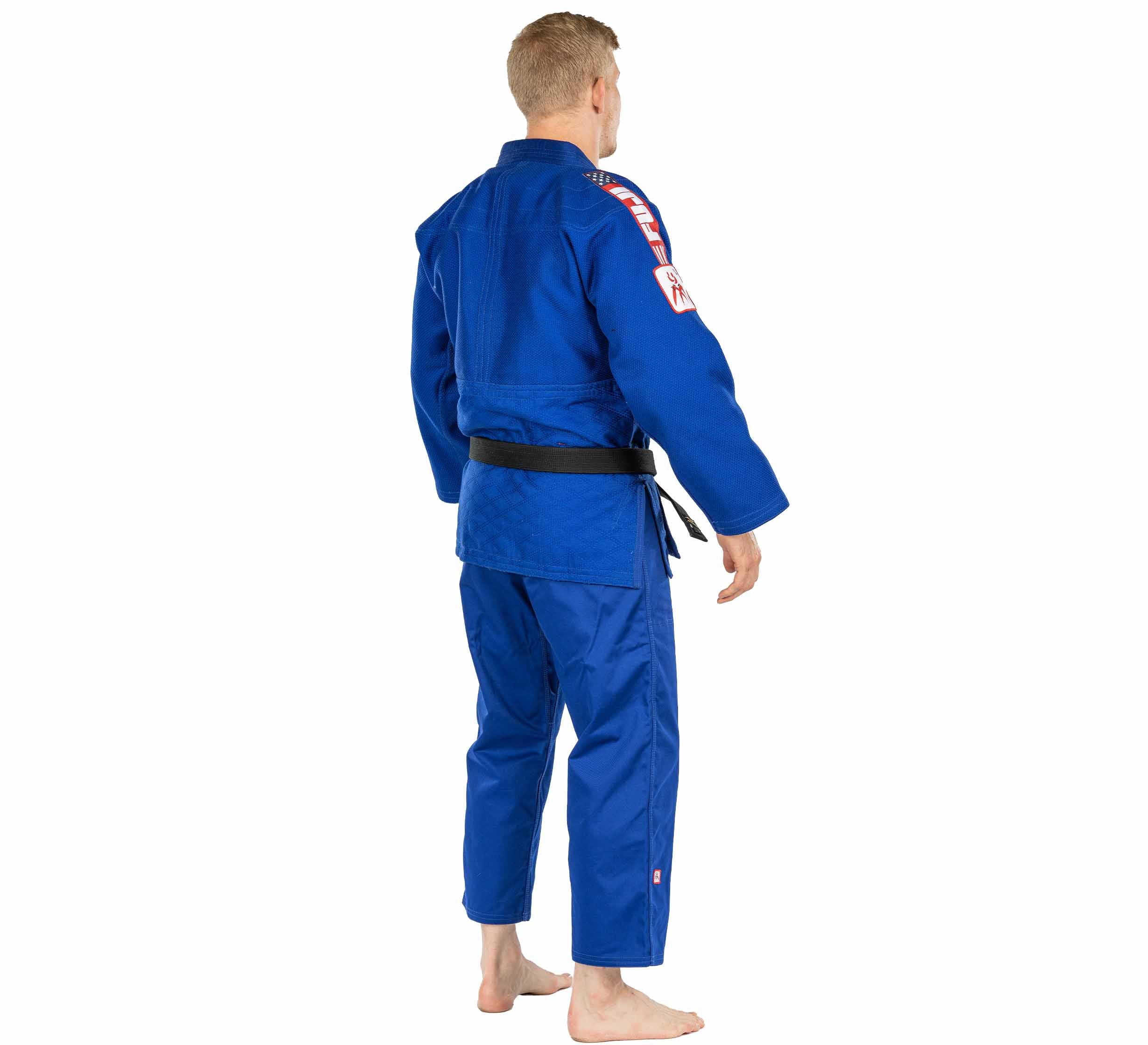 A person with short blond hair, barefoot and facing away on a white background, wears the USA Judo Single Weave Gi 2.0 Blue with a black belt.