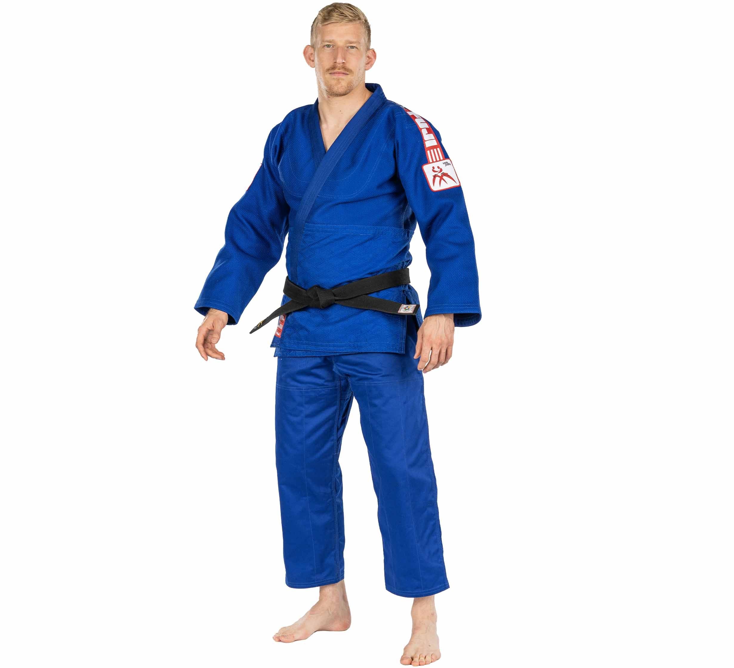 A man stands barefoot, wearing a USA Judo Double Weave Gi 2.0 Blue with a black belt and red and white sleeve patches. He faces forward against a white background.