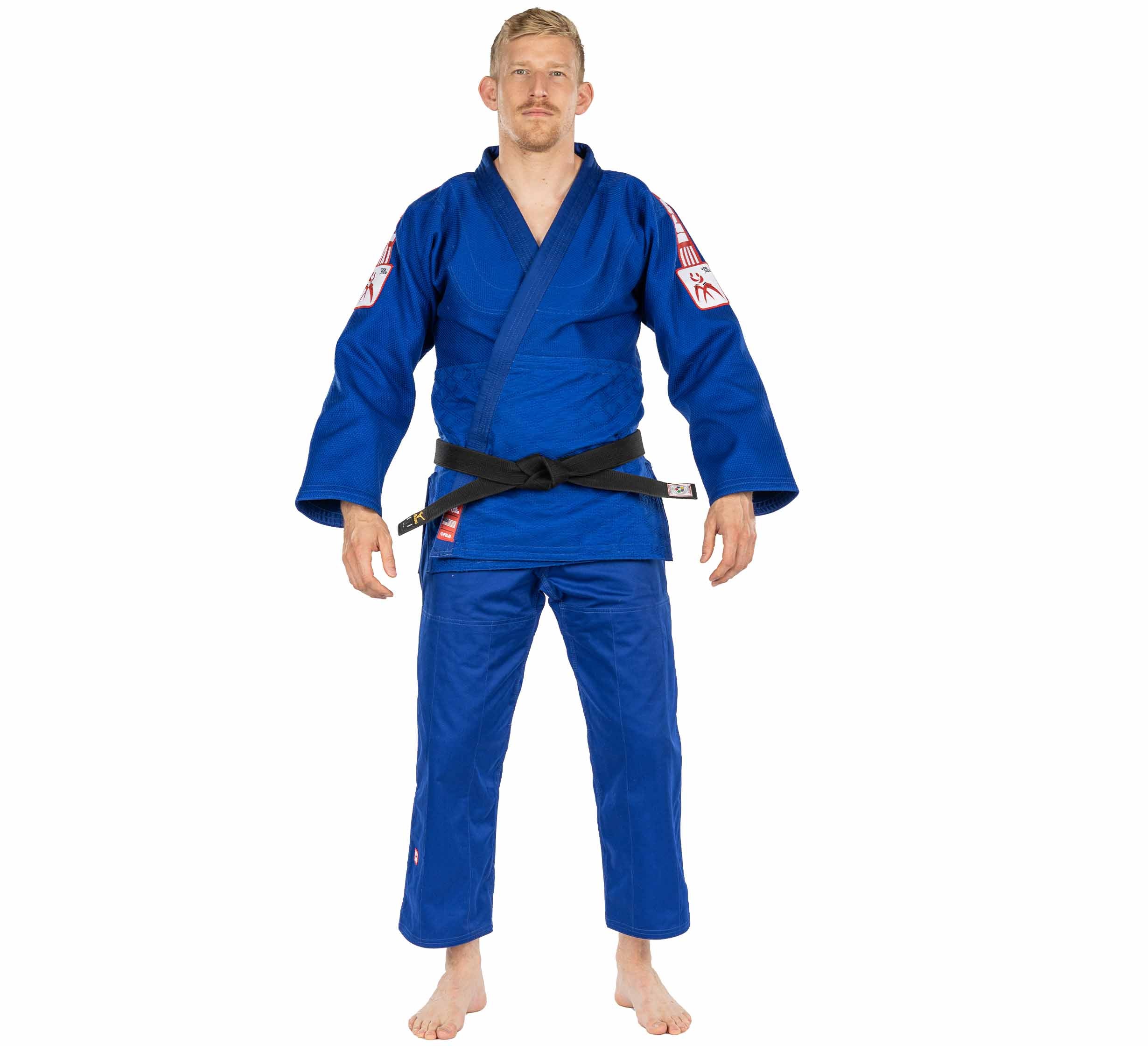 A man stands barefoot, wearing the blue USA Judo Single Weave Judo Gi with white and red patches on the shoulders and legs, paired with a black belt. He faces forward against a plain white background.
