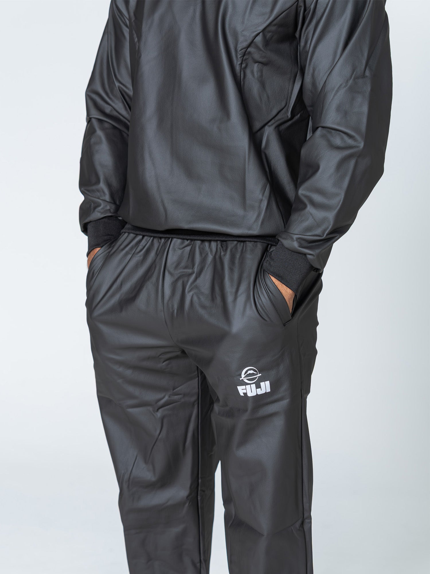 A person wearing the Grappling Sauna Suit Black with hands in pockets. The suit features a FUJI logo on the left thigh, and the person's head is not visible in the image.